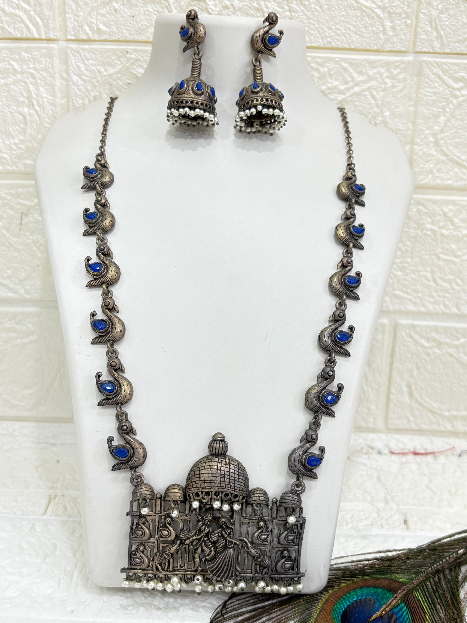Name:
Heritage Dandiya Dome Necklace Set Oxidised silver necklace with temple-style dome pendant featuring dandiya dance motifs, accented with blue stone paisleys and matching jhumka earrings.