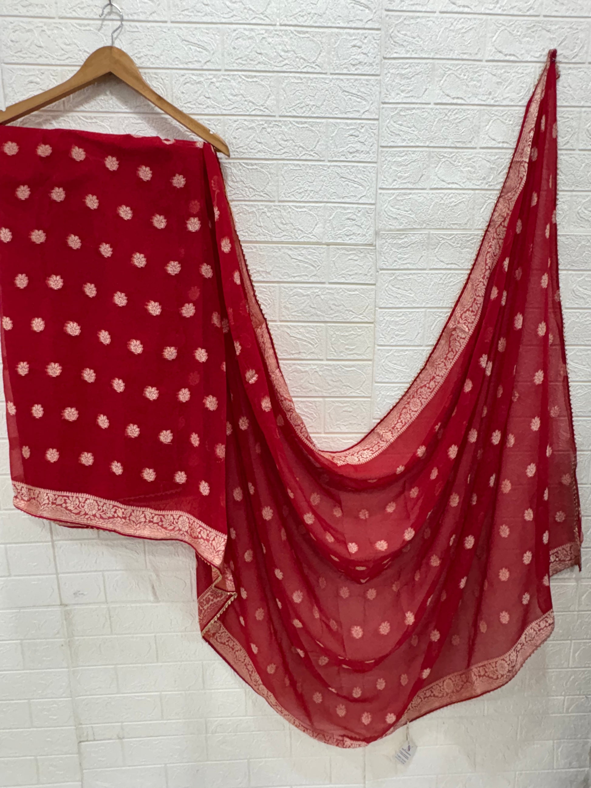 This fabric is a red Georgette with all-over gold zari floral buti embroidery and a rich woven border, paired with a matching plain blouse perfect for festival