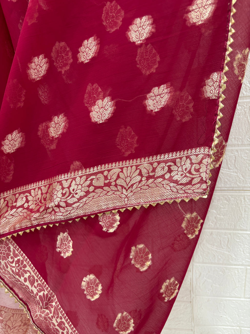 This fabric is a maroon soft Georgette with all over gold zari floral buti embroider and a rich woven border paired with a matching plain blouse perfect for festival
