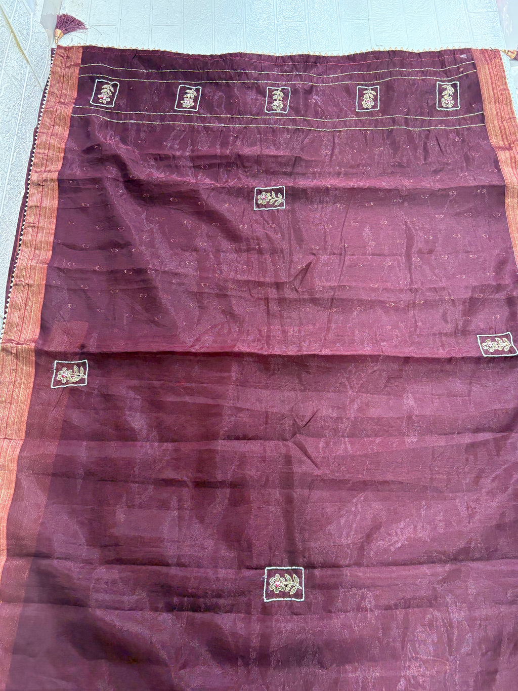 Name: Chanderi or Cotton Silk Saree Fabric The fine texture, sheen, and way the material is folded suggest a Chanderi or Cotton Silk Blend. The work is Zari Woven Stripes with Aari/Thread Embroidery motifs.