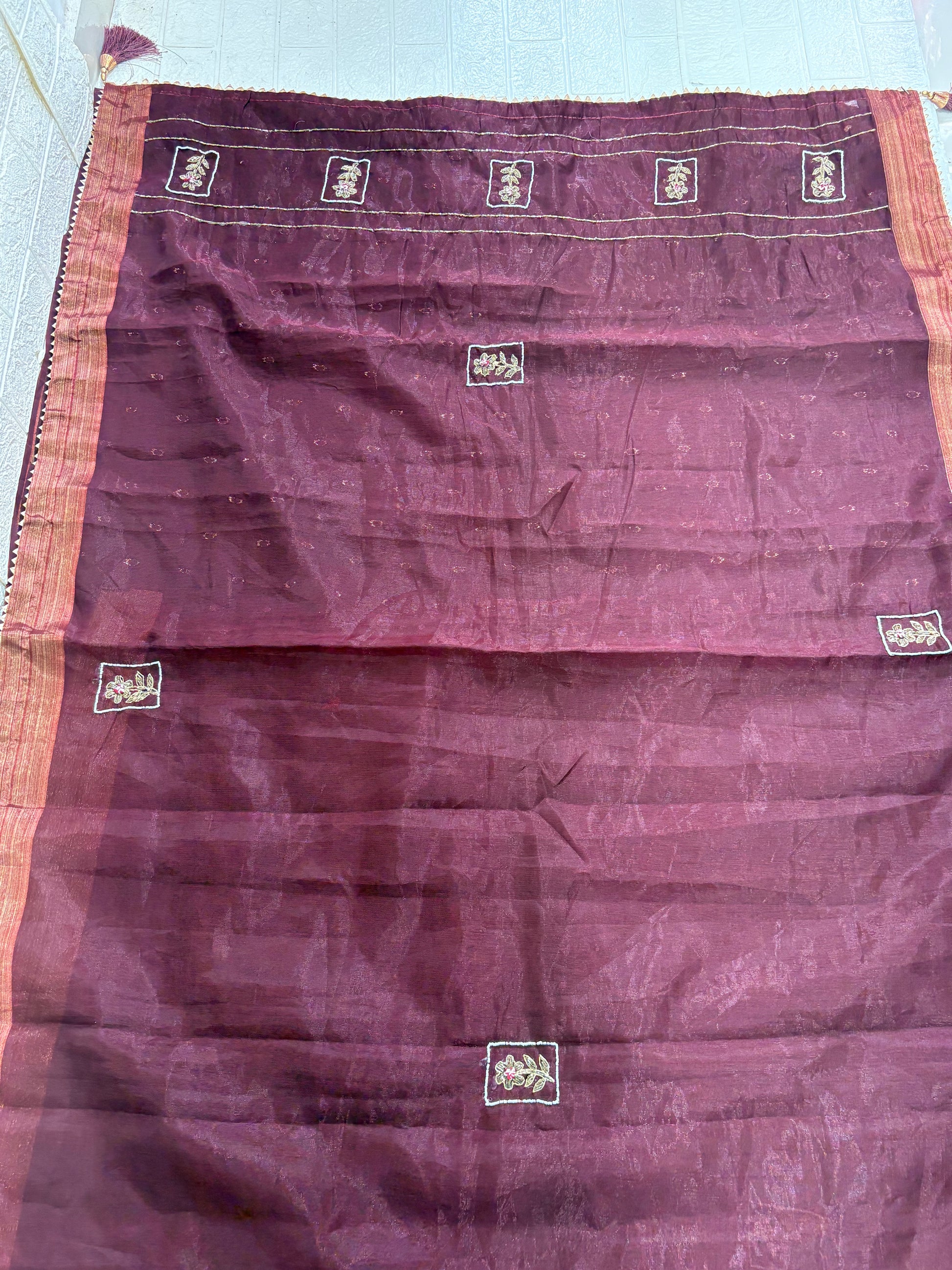 Name: Chanderi or Cotton Silk Saree Fabric The fine texture, sheen, and way the material is folded suggest a Chanderi or Cotton Silk Blend. The work is Zari Woven Stripes with Aari/Thread Embroidery motifs.